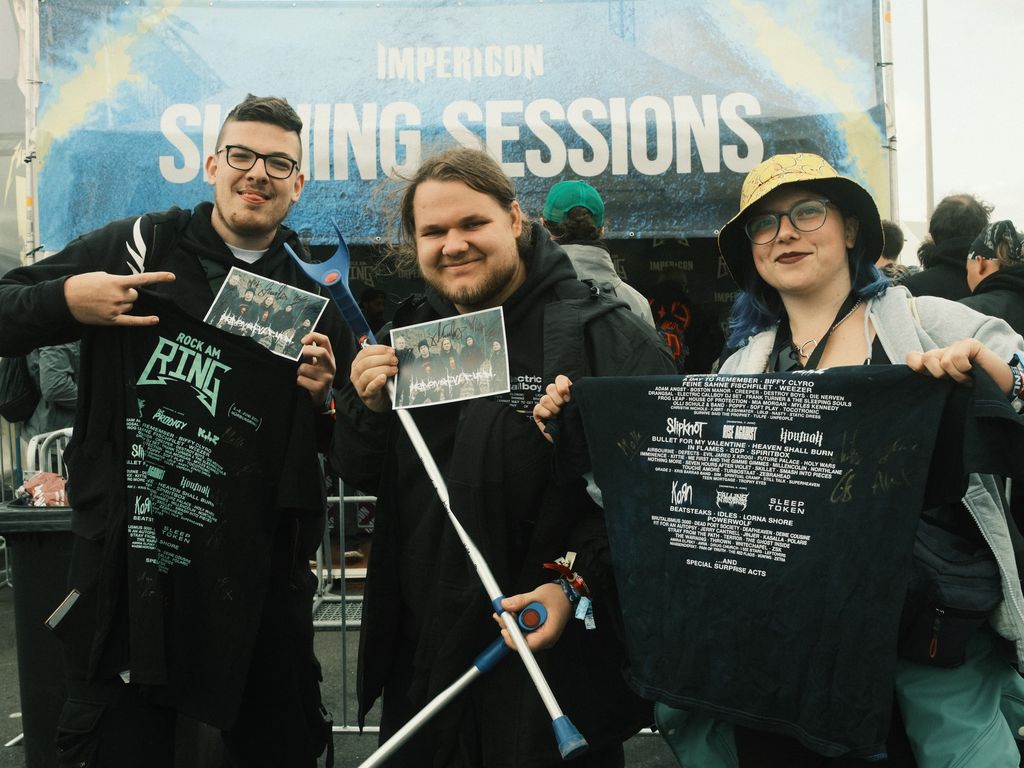 Three fans are holding signed autograph cards and T-shirts up to the camera