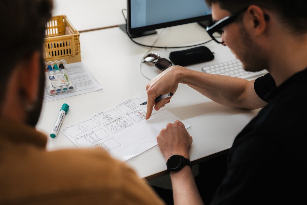 Two people discussing a drawn-up plan on a desk